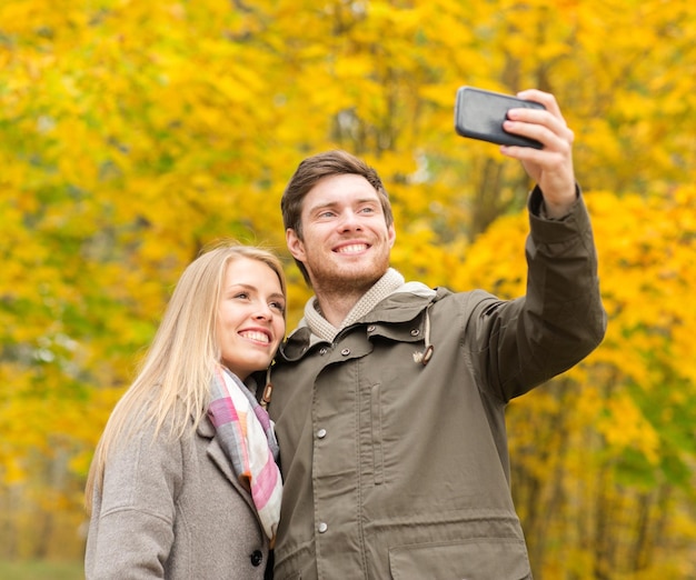 concetto di amore, relazione, famiglia e persone - coppia sorridente che si abbraccia e si fa selfie nel parco autunnale