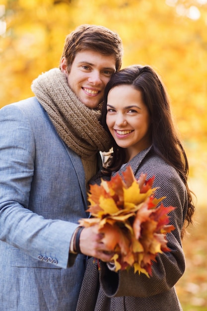 concetto di amore, relazione, famiglia e persone - coppia sorridente con un mazzo di foglie che si abbracciano nel parco autunnale