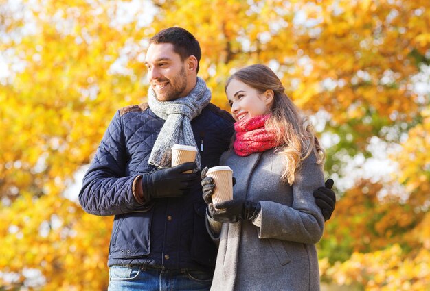 concetto di amore, relazione, stagione, amicizia e persone - coppia sorridente con tazze di caffè nel parco autunnale