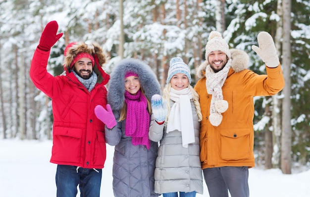 concetto di amore, relazione, stagione, amicizia e persone - gruppo di uomini e donne sorridenti che agitano le mani nella foresta invernale