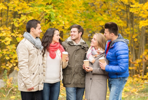 concetto di amore, relazione, stagione, amicizia e persone - gruppo di uomini e donne sorridenti che camminano con tazze di caffè di carta nel parco autunnale