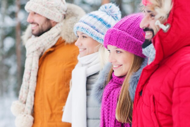 concetto di amore, relazione, stagione, amicizia e persone - gruppo di uomini e donne sorridenti che camminano nella foresta invernale