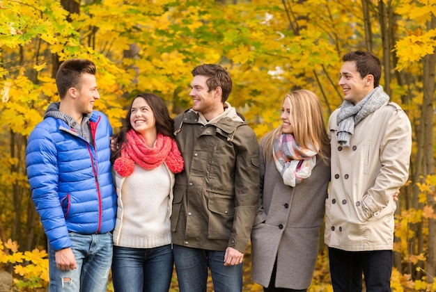 concetto di amore, relazione, stagione, amicizia e persone - gruppo di uomini e donne sorridenti che si abbracciano nel parco autunnale