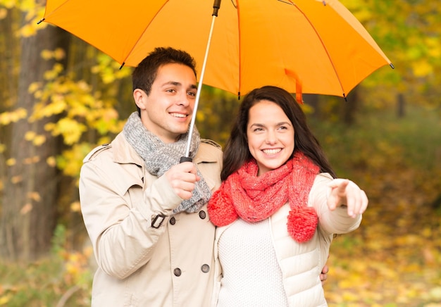 concetto di amore, relazione, stagione, famiglia e persone - coppia sorridente con ombrello che cammina nel parco autunnale