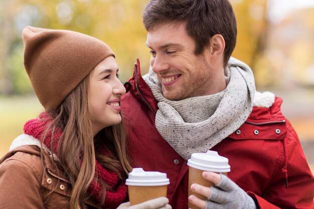 concetto di amore, relazioni, stagione e persone - giovane coppia felice con tazze di caffè che camminano nel parco autunnale
