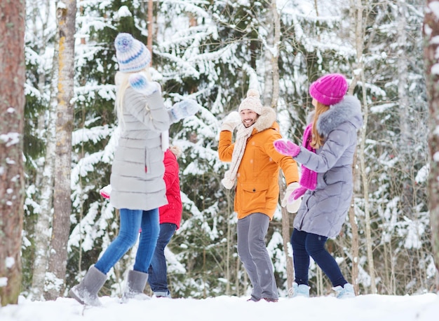 concetto di amore, stagione, amicizia, intrattenimento e persone - gruppo di uomini e donne felici che si divertono e giocano a palle di neve nella foresta invernale