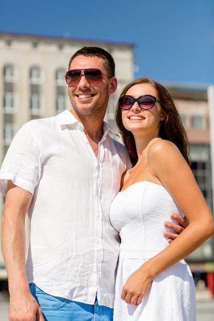 concetto di amore, viaggi, turismo, persone e amicizia - coppia sorridente che indossa occhiali da sole che si abbracciano in città