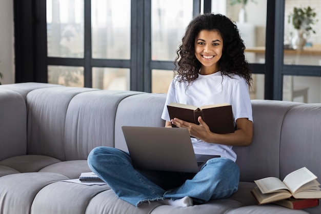 Concetto di apprendimento online. Ritratto giovane studentessa afroamericana studio a casa utilizzando il computer portatile, sorridente, guardando la telecamera. Didattica a distanza a domicilio