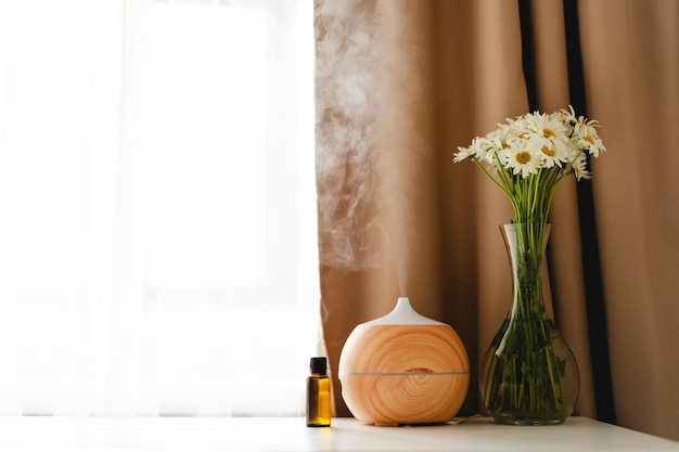 Concetto di aromaterapia Diffusore di olio aromatico sul tavolo contro la finestra Deodorante per ambienti Diffusore di aromi ad ultrasuoni per la casa