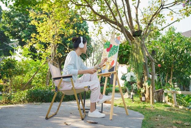 Concetto di arte creativa L'artista femminile tiene il pennello e dipinge l'immagine su tela mentre ascolta la musica