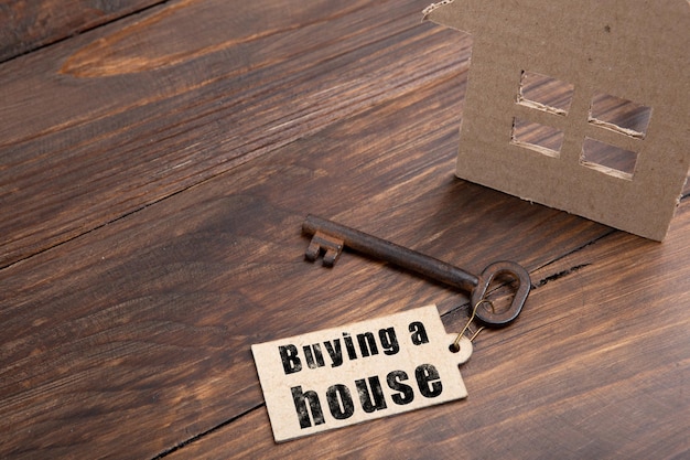 Concetto di assicurazione immobiliare vecchia chiave con etichetta e casa di cartone su sfondo di legno