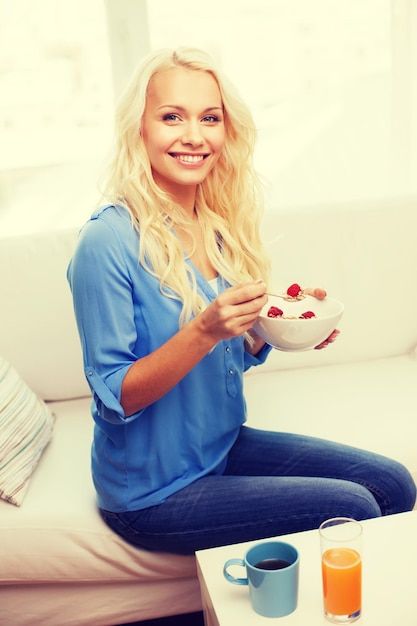 concetto di assistenza sanitaria, cibo, casa e felicità - donna sorridente con una ciotola di muesli che fa colazione a casa