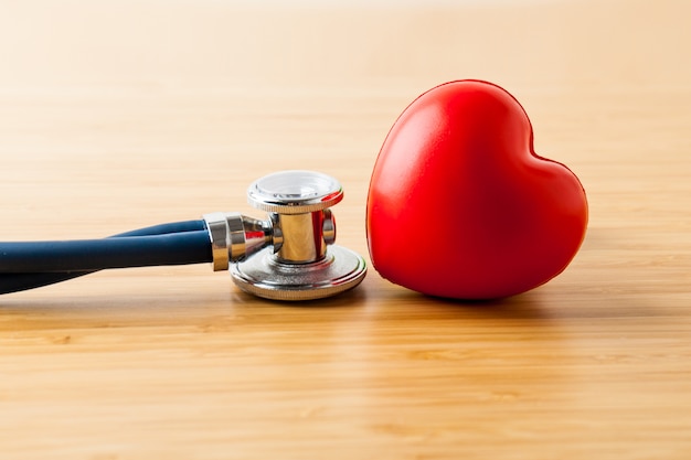 Concetto di assistenza sanitaria e medica. Stetoscopio e cuore rosso sul tavolo di legno.