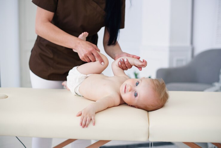 Concetto di assistenza sanitaria e medica. Una massaggiatrice professionista fa un massaggio e una ginnastica a un bambino piccolo nella moderna sala accogliente.