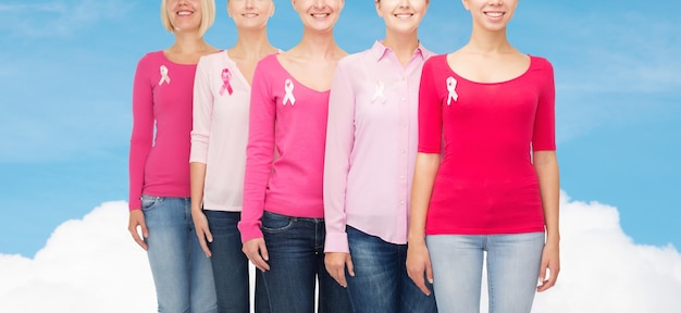 concetto di assistenza sanitaria, persone e medicina - primo piano di donne sorridenti in camicie bianche con nastri rosa per la consapevolezza del cancro al seno su cielo blu e sfondo bianco nuvola