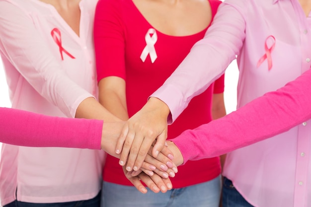 concetto di assistenza sanitaria, persone, gesto e medicina - primo piano di donne in camicie bianche con nastri rosa per la consapevolezza del cancro al seno che mettono le mani in cima su sfondo bianco