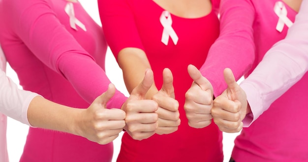 concetto di assistenza sanitaria, persone, gesto e medicina - primo piano di donne in camicie bianche con nastri rosa per la consapevolezza del cancro al seno che mostrano i pollici in su su sfondo bianco