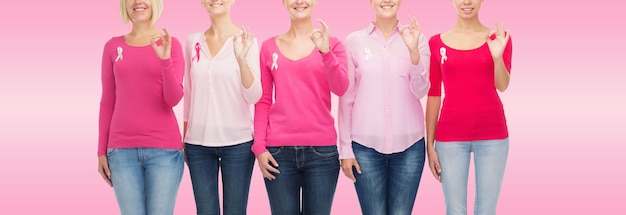 concetto di assistenza sanitaria, persone, gesto e medicina - primo piano di donne sorridenti in camicie bianche con nastri di consapevolezza del cancro al seno che mostrano segno ok su sfondo rosa