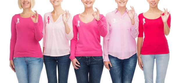 concetto di assistenza sanitaria, persone, gesto e medicina - primo piano di donne sorridenti in camicie bianche con nastri rosa per la consapevolezza del cancro al seno che mostrano segno ok su sfondo bianco