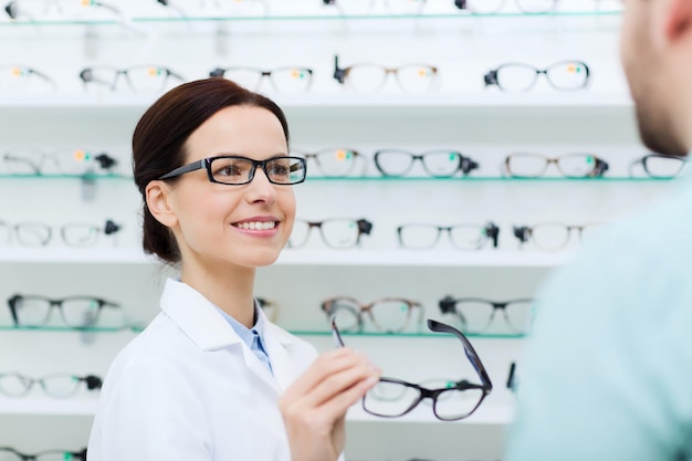 concetto di assistenza sanitaria, persone, vista e visione - ottico femminile che mostra gli occhiali all'uomo al negozio di ottica