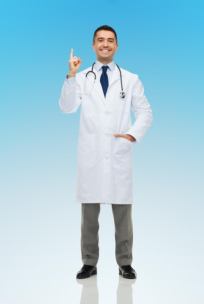 concetto di assistenza sanitaria, professione, persone e medicina - medico maschio sorridente felice in camice bianco che punta il dito su sfondo blu