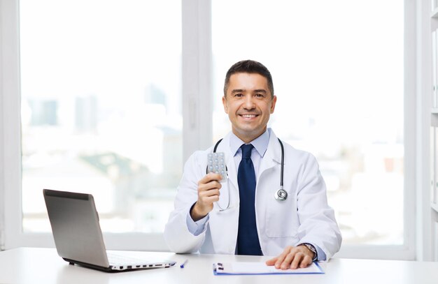 concetto di assistenza sanitaria, professione, persone e medicina - medico maschio sorridente in camice bianco con tablet e computer portatile in studio medico