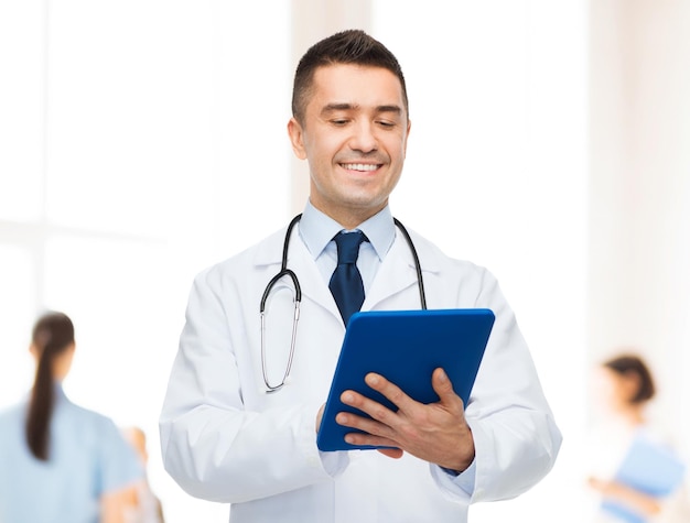 concetto di assistenza sanitaria, professione, persone e medicina - medico maschio sorridente in camice bianco con tablet pc su un gruppo di medici sullo sfondo dell'ospedale