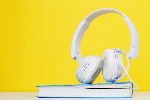 Concetto di audiolibro con moderne cuffie bianche e libro con copertina rigida su sfondo giallo