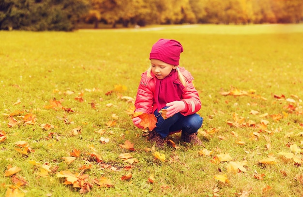 concetto di autunno, infanzia, felicità e persone - bambina felice che raccoglie foglie d'acero all'aperto