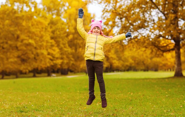concetto di autunno, infanzia, felicità e persone - bambina felice con le mani alzate che salta e si diverte all'aperto