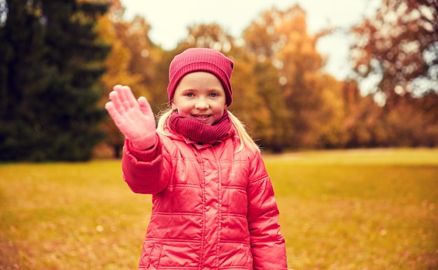 concetto di autunno, infanzia, gesto, natura e persone - bambina felice che agita la mano nel parco