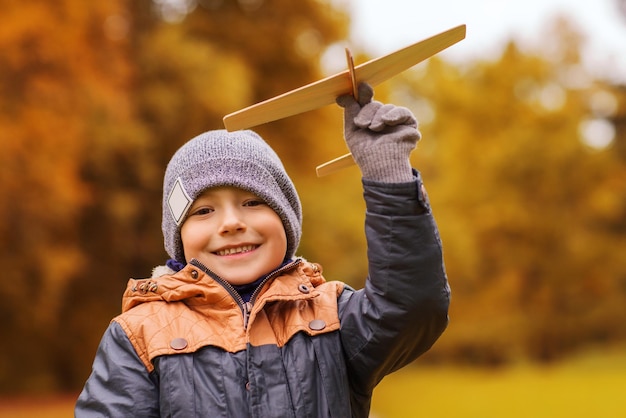 concetto di autunno, infanzia, sogno, tempo libero e persone - ragazzino felice che gioca con l'aereo giocattolo in legno all'aperto