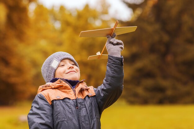 concetto di autunno, infanzia, sogno, tempo libero e persone - ragazzino felice che gioca con l'aereo giocattolo in legno all'aperto