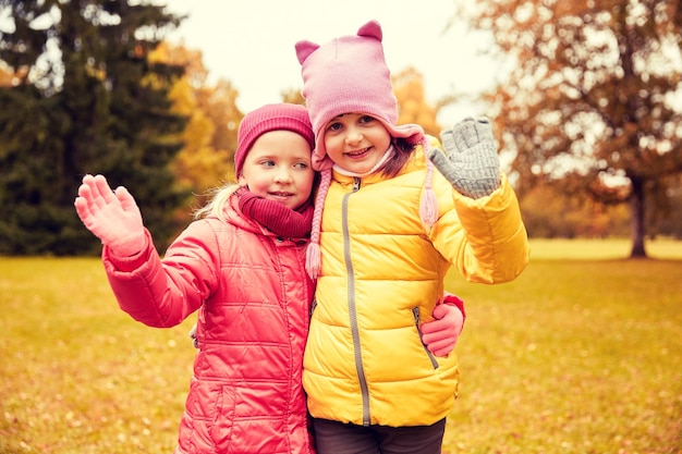 concetto di autunno, infanzia, tempo libero e persone - due bambine felici che agitano la mano nel parco autunnale