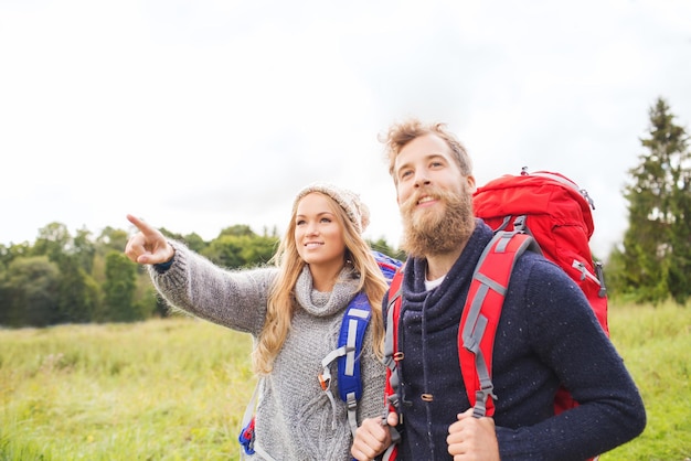 concetto di avventura, viaggi, turismo, escursione e persone - coppia sorridente che cammina con gli zaini all'aperto