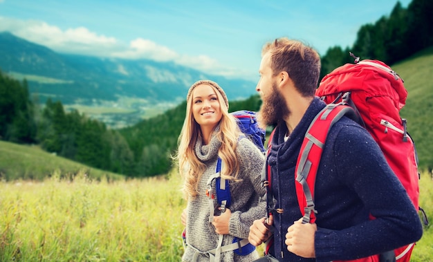 concetto di avventura, viaggi, turismo, escursione e persone - coppia sorridente che cammina con gli zaini su sfondo di colline alpine