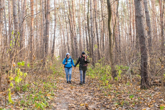 Concetto di avventura, viaggi, turismo, escursione e persone - coppia sorridente che cammina con gli zaini sulla superficie naturale autunnale