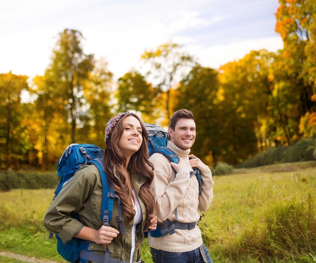 concetto di avventura, viaggio, turismo, escursione e persone - coppia sorridente che cammina con gli zaini su sfondo naturale