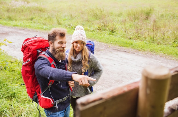 concetto di avventura, viaggio, turismo, escursione e persone - coppia sorridente con zaini in piedi al cartello all'aperto