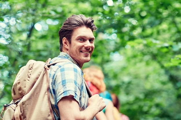 concetto di avventura, viaggio, turismo, escursione e persone - gruppo di amici sorridenti che camminano con gli zaini nei boschi