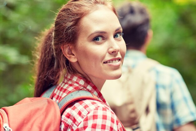 concetto di avventura, viaggio, turismo, escursione e persone - gruppo di amici sorridenti che camminano con gli zaini nei boschi