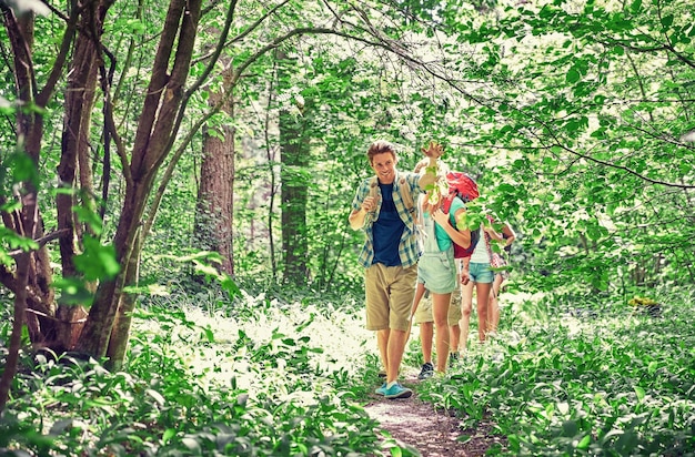 concetto di avventura, viaggio, turismo, escursione e persone - gruppo di amici sorridenti che camminano con gli zaini nei boschi