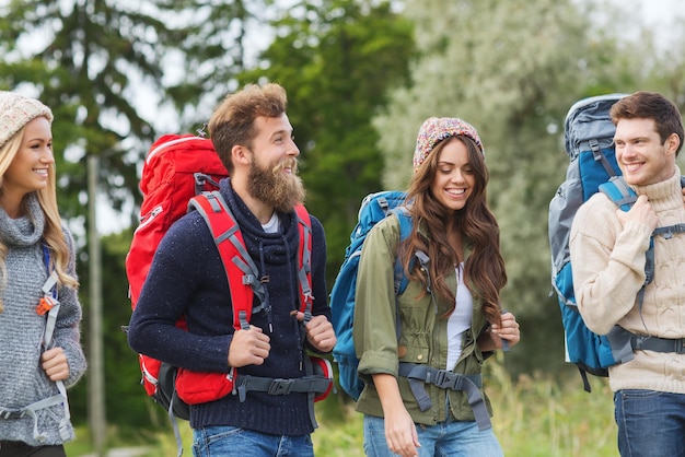 concetto di avventura, viaggio, turismo, escursione e persone - gruppo di amici sorridenti che camminano con gli zaini