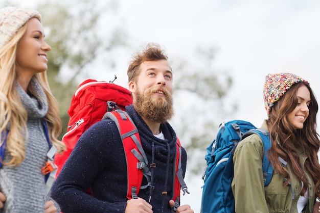 concetto di avventura, viaggio, turismo, escursione e persone - gruppo di amici sorridenti che camminano con gli zaini