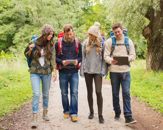 concetto di avventura, viaggio, turismo, escursione e persone - gruppo di amici sorridenti con zaini e computer tablet pc che camminano all'aperto