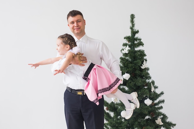 Concetto di bambini, festivi e vacanze - padre e figlia che hanno divertimento vicino all'albero di Natale
