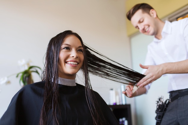 concetto di bellezza, acconciatura e persone - giovane donna felice e parrucchiere che tagliano le punte dei capelli al salone