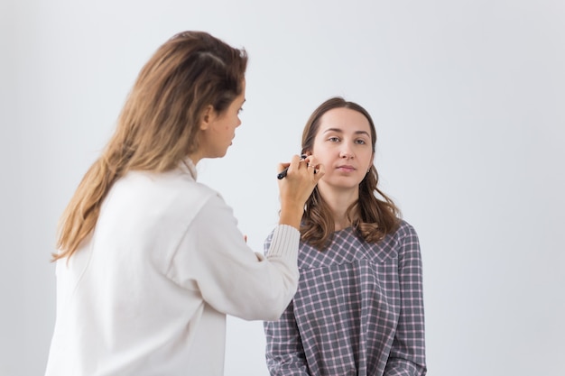 Concetto di bellezza e cosmetici - artista di trucco che fa trucco professionale di giovane donna.