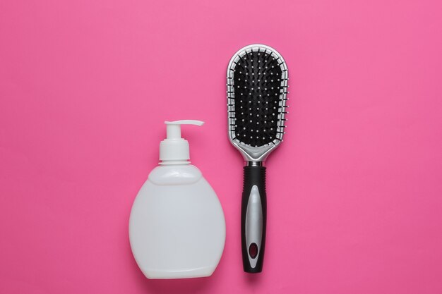 Concetto di bellezza minimalista Cura dei capelli Pettine e bottiglia di shampoo su sfondo rosa