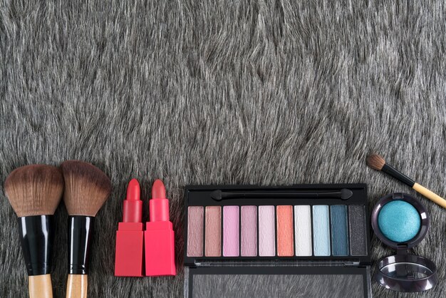 Concetto di bellezza: palette di ombretti, pennelli per il trucco e rossetti su pelliccia finta grigia